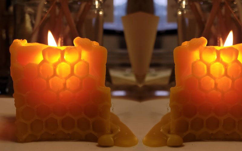 Op deze afbeelding ziet u twee brandende bijenwaskaarsen die je hier kunt kopen. Het zijn waskaarsen van echte bijenwas met extra branduren.